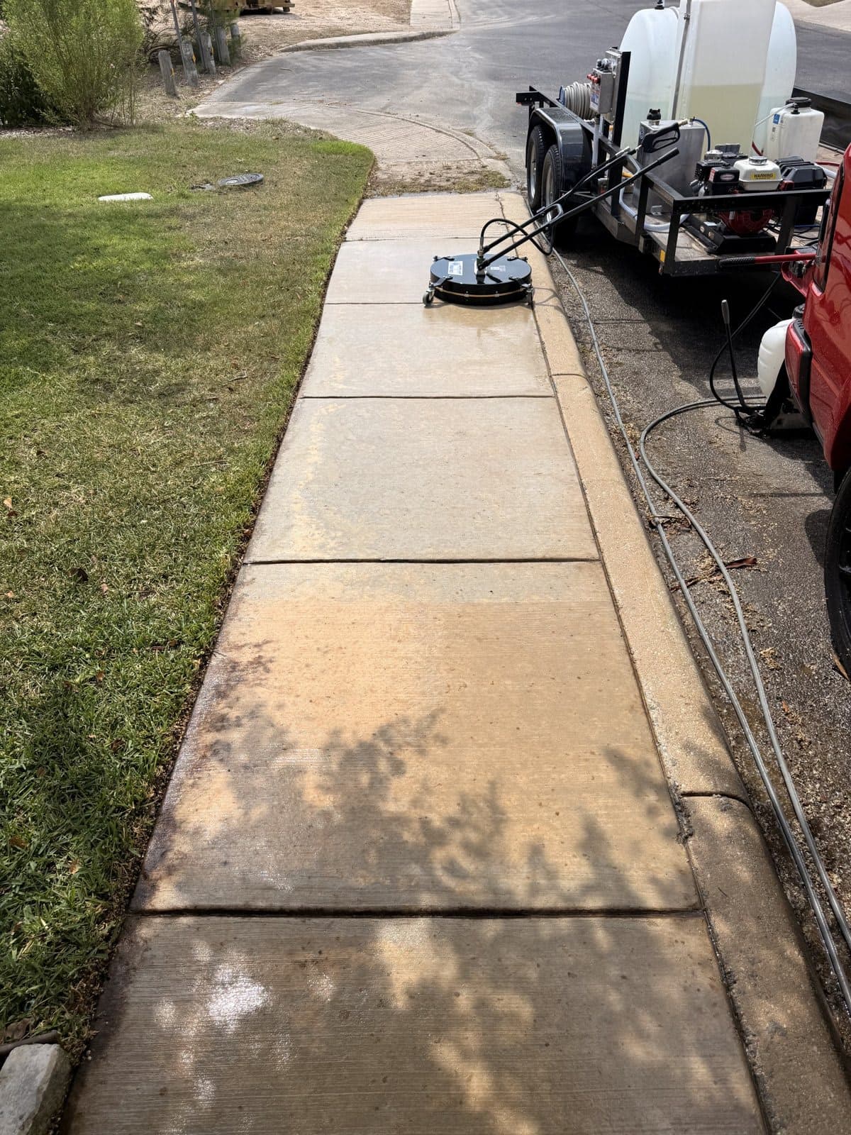 Surface cleaner running across a residential walkway mid-job, with the Torres work truck and pressure washing rig behind it